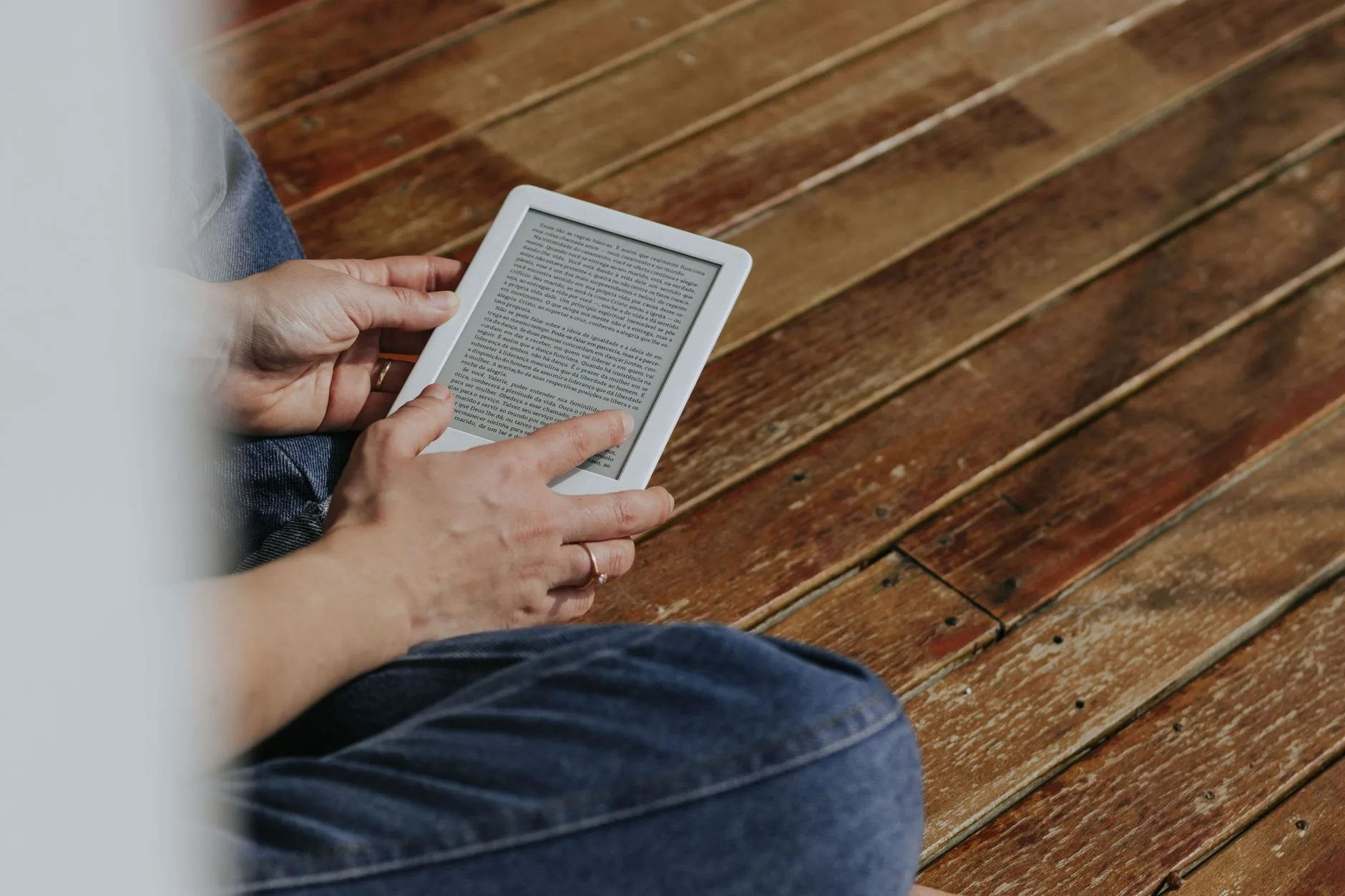 Isca digital ou ebook — Close de mãos segurando um leitor eletrônico em um piso de madeira, retratando um momento de lei